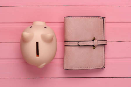 Piggy bank with leather wallet on pink wooden background. Top viewの写真素材