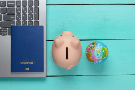 Traveling idea. Online travel. Laptop with piggy bank, passport, globe on a blue wooden background. Top viewの写真素材