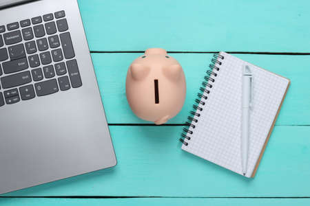 Piggy Bank With Laptop, Notebook on blue wooden background. Make money online or internet business concepts. Top view. Flat layの写真素材