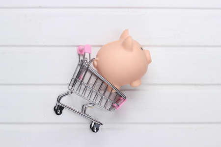 Shopping concept, economy. Piggy bank with supermarket trolley on white wooden background. Top viewの写真素材