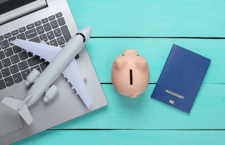 Traveling idea. Online travel. Laptop with piggy bank, passport, plane on a blue wooden background. Top viewの写真素材