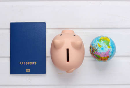 Travel or emigration. Passport with piggy bank, globe on white wooden background. Top view. Flat layの写真素材
