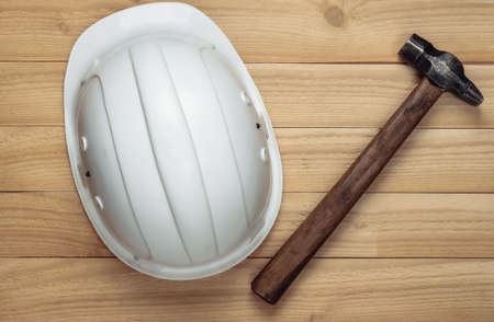 White construction safety helmet with hammer on wooden background. Engineering, construction concept. Top view.の写真素材