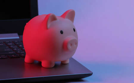 Piggy bank on laptop keyboard. Neon gradient red-blue, ultraviolet light. Make money online or internet businessの写真素材