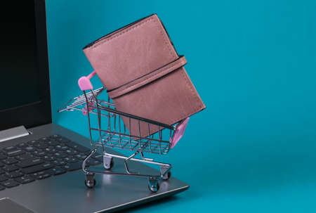 Mini supermarket trolley with wallet on laptop keyboard. Blue studio background. Online shoppingの写真素材