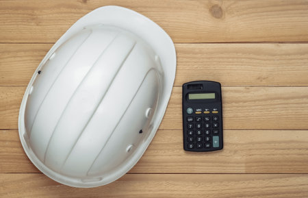White construction safety helmet with calculator on wooden background. Engineering, construction concept. Top view.の写真素材
