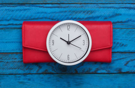 Time to make money. White clock and wallet on blue wooden background. Minimalistic studio shot. Top viewの写真素材