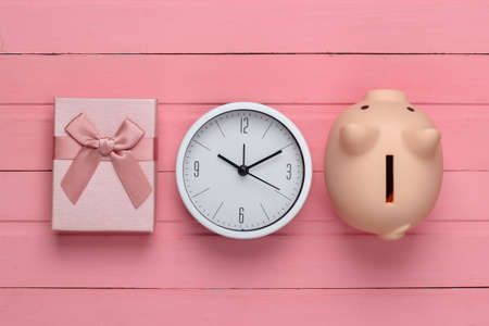 Gift boxes with clock, piggy bank on pink wooden background. Top viewの写真素材