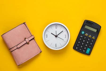 Time to make money. White clock, calculator and wallet on yellow background. Minimalistic studio shot. Top viewの写真素材