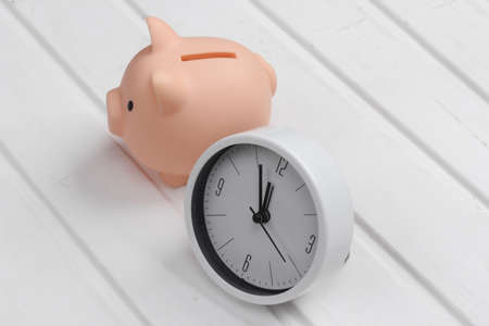 Time to invest. White clock and piggy bank on white wooden backgroundの写真素材