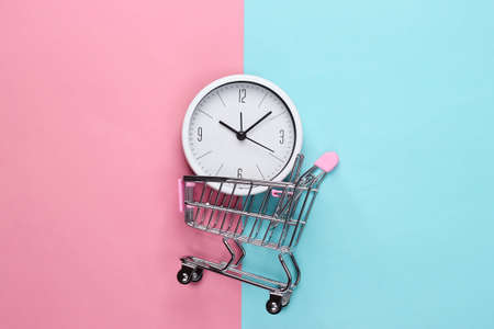 Shopping time. Supermarket trolley with clock on pink blue background. Minimalism. Top view