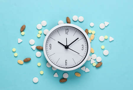 Time to take pills. White clock with pills on blue pastel background. Top view. Flat layの写真素材