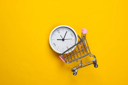 Shopping time. Supermarket trolley with clock on a yellow background. Minimalism. Top viewの写真素材