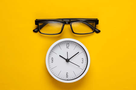 White clock with glasses on yellow background. Top viewの写真素材