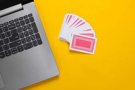 Playing Cards and laptop keyboard on yellow background. Online poker casino. Top view