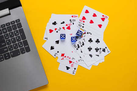 Playing Cards and Blue Dice, laptop keyboard on yellow background. Online poker casino. Top view