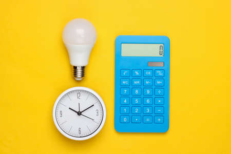 Clock with light bulb, calculator on a yellow background. Minimalism. Top viewの写真素材