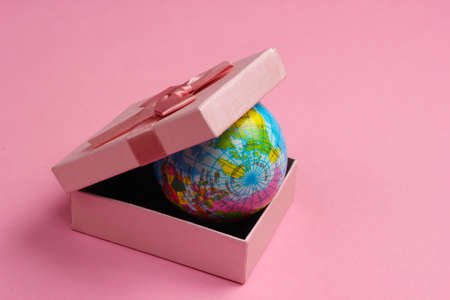 Globe in a gift box on a pink background.