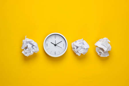 Clock with crumpled paper balls on a yellow background. Top viewの写真素材
