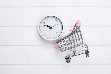 Shopping time. Supermarket trolleys with clock on white wooden background. Minimalism. Top viewの写真素材
