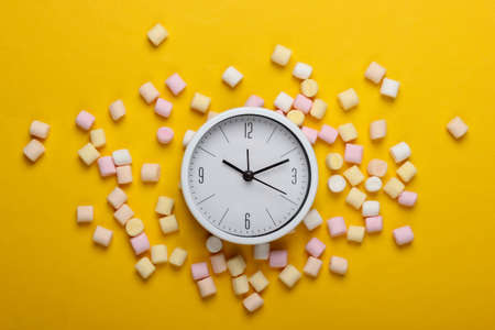 white clock with marshmallows on a yellow background. Top view. Pop art, minimalismの写真素材