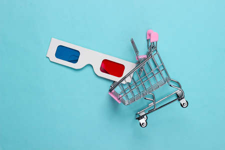 Anaglyph disposable paper 3d glasses in mini shopping trolley on blue background. Top view
