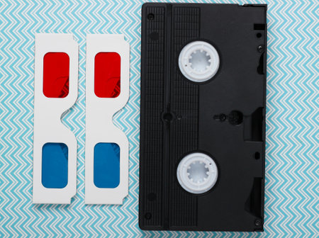 Retro 80s paper stereo 3D glasses and video cassette. Blue pastel background. Top view