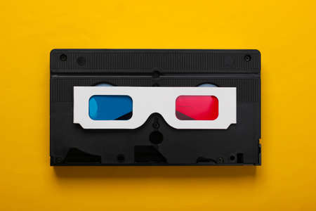 Anaglyph disposable paper 3d glasses and video cassette on yellow background. Retro media,...