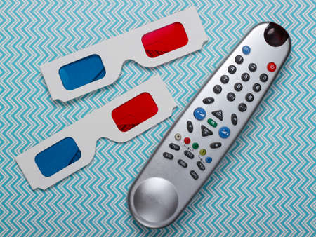 Anaglyph disposable paper 3d glasses and tv remote on blue background. Tv time. Top viewの写真素材