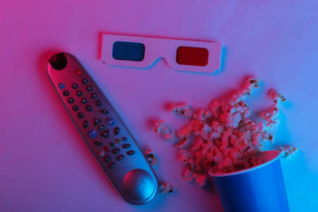 ovie time. Cardboard bucket of popcorn, tv remote and Stereoscopic anaglyph disposable paper 3d glasses in pink blue gradient neon light. Top viewの写真素材