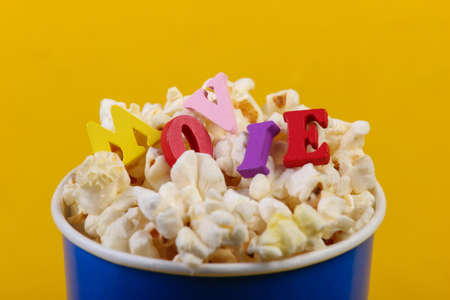 Movie time. Cardboard bucket of popcorn with word movie on yellow background.の写真素材