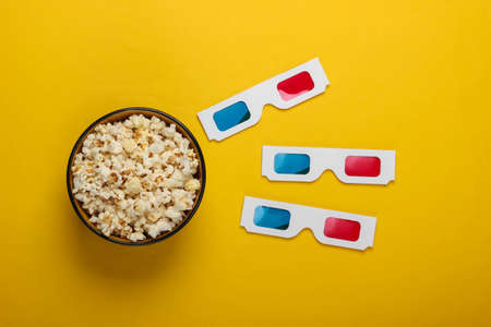 Movie time. Stereoscopic anaglyph disposable paper 3d glasses and popcorn bowl on yellow pastel background. Top viewの写真素材