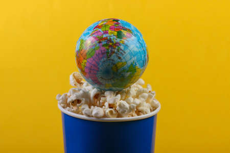 Global movie premiere. Cinema. Movie time. Cardboard bucket of popcorn with globe on yellow...