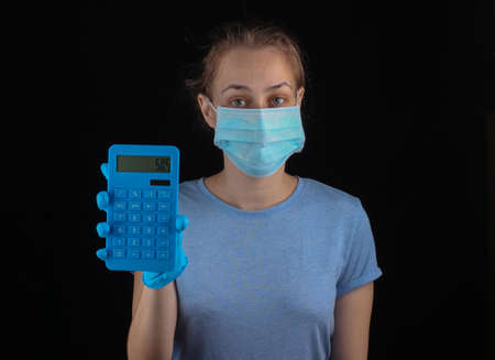 Woman in a medical protective mask, gloves hold calculator on a black background.