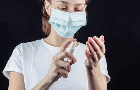 Woman in a median face mask disinfects hands with an antiseptic on a black background.