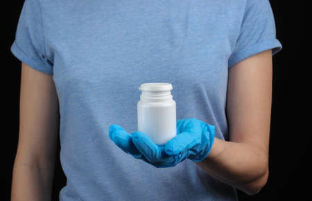 Woman in medical gloves holds a bottle of pills on black background
