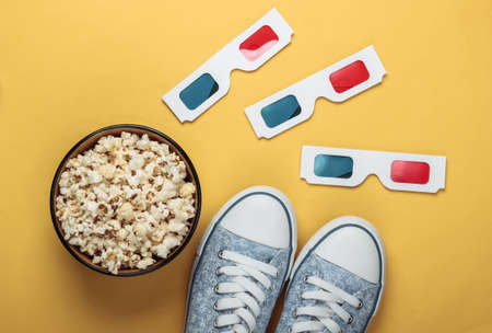 Anaglyph disposable paper 3d glasses with old school style sneakers and popcorn bowl on yellow background. Top view. Retro 80sの写真素材