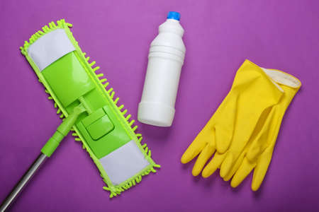 Cleaning products. Plastic green mop, gloves, bottle of detergent on purple background. Disinfection...