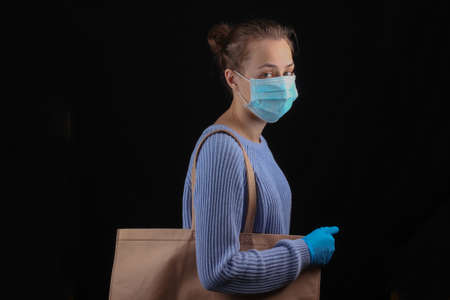 Shopping during the  pandemic. Woman in medical mask and gloves holds a bag for shopping in...