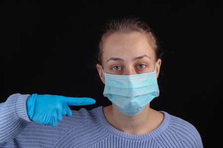 Stop the covid-19 pandemic. Woman in gloves points to a medical mask on her face on a black backgroundの写真素材
