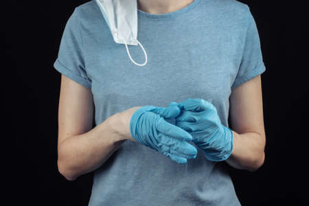 Woman takes off medical gloves on a black background. Overcoming the pandemic