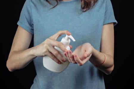 Woman disinfects hands with an antiseptic on a black background. Hygiene in covid-19 pandemic