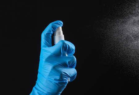 Hand in a medical glove sprays a bottle of antiseptic spray on a black backgroundの写真素材