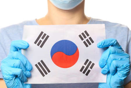 Pandemic covid-19 theme. Woman in protective gloves, medical face mask holds Korea flag isolated on white background.の写真素材