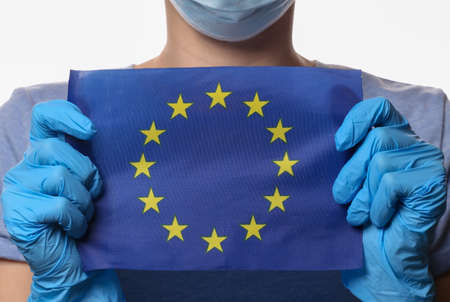 Pandemic theme. Woman in protective gloves, medical face mask holds Euro Union flag isolated on...