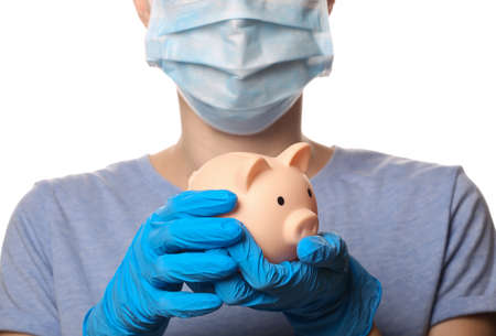 Woman in media mask and gloves holds piggy bank isolated on white backgroundの写真素材