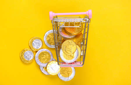 Shopping theme. Mini Supermarket trolley with coins on yellow background.の写真素材
