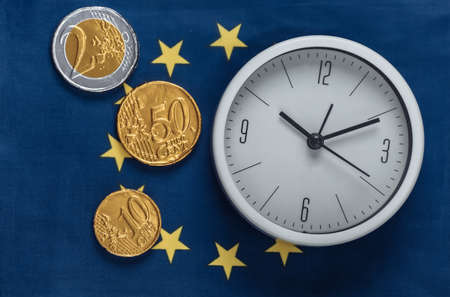 White clock with coins on the background of the Euro Union flagの写真素材