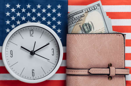 Leather wallet with hundred dollar bills, clock on background of USA flag. Time is moneyの写真素材