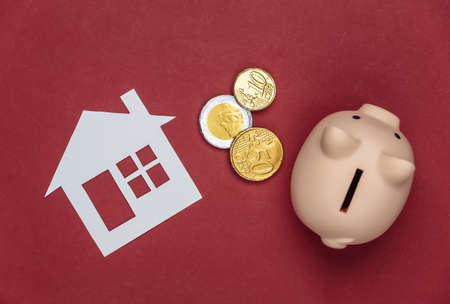 Paper house and piggy bank with coins on a red background.の写真素材